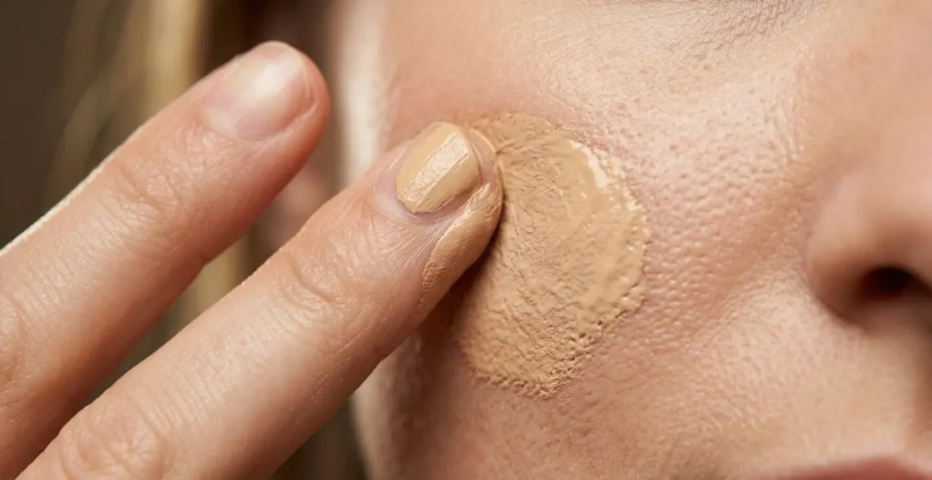 Mains expertes appliquant un fond de teint bio par gestes de tapotements délicats sur une peau